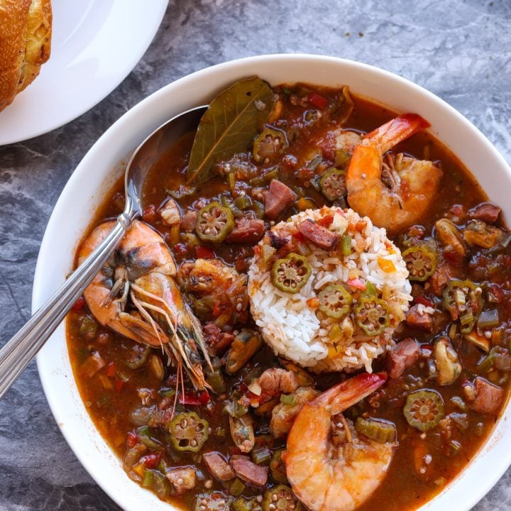 Okra gumbo with shrimp in a white bowl with bread rolls