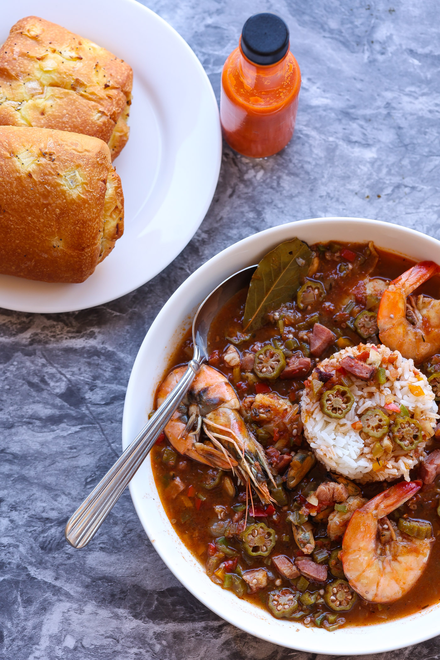Okra gumbo with shrimp in a white bowl with bread rolls