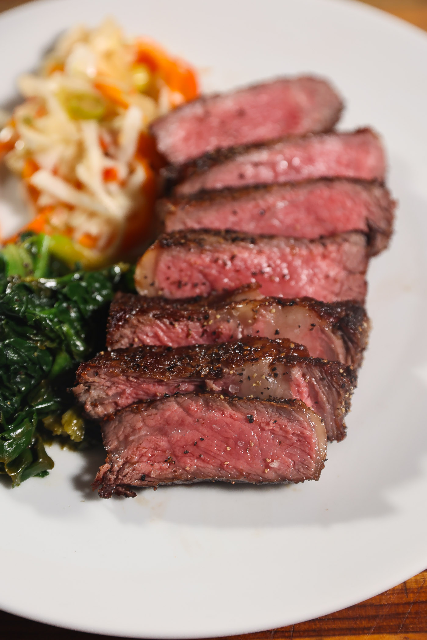 sliced reverse seared ribeye steak on a plate with cabbage and spinach