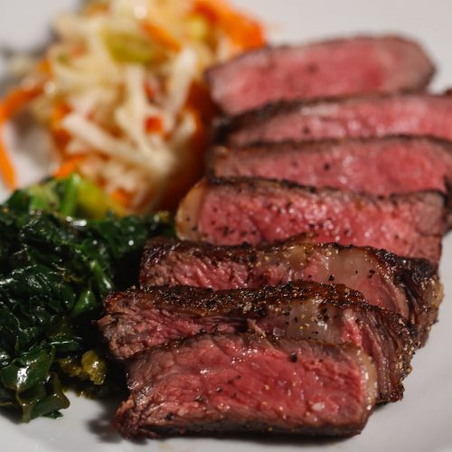 sliced reverse seared ribeye steak on a plate with cabbage and spinach