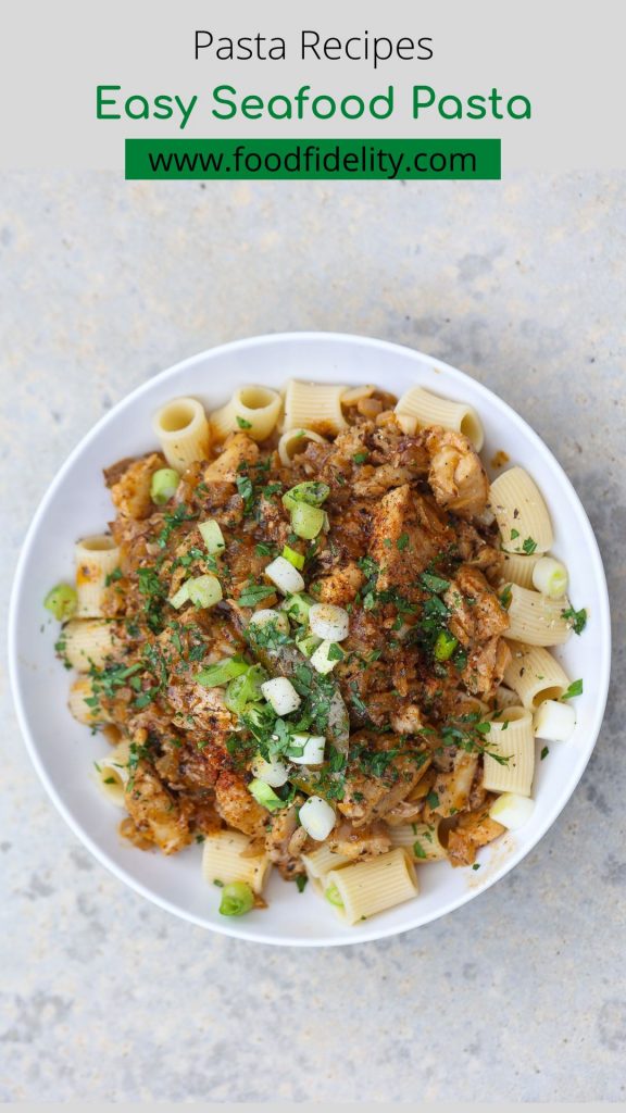 seafood pasta topped with green onions in a white bowl