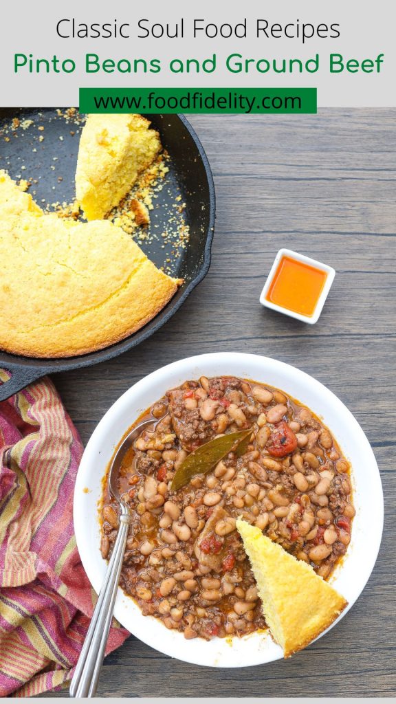 A photo of a bowl of cooked pinto beans with a garnish of a cornbread slice and small bowl of hot sauce
