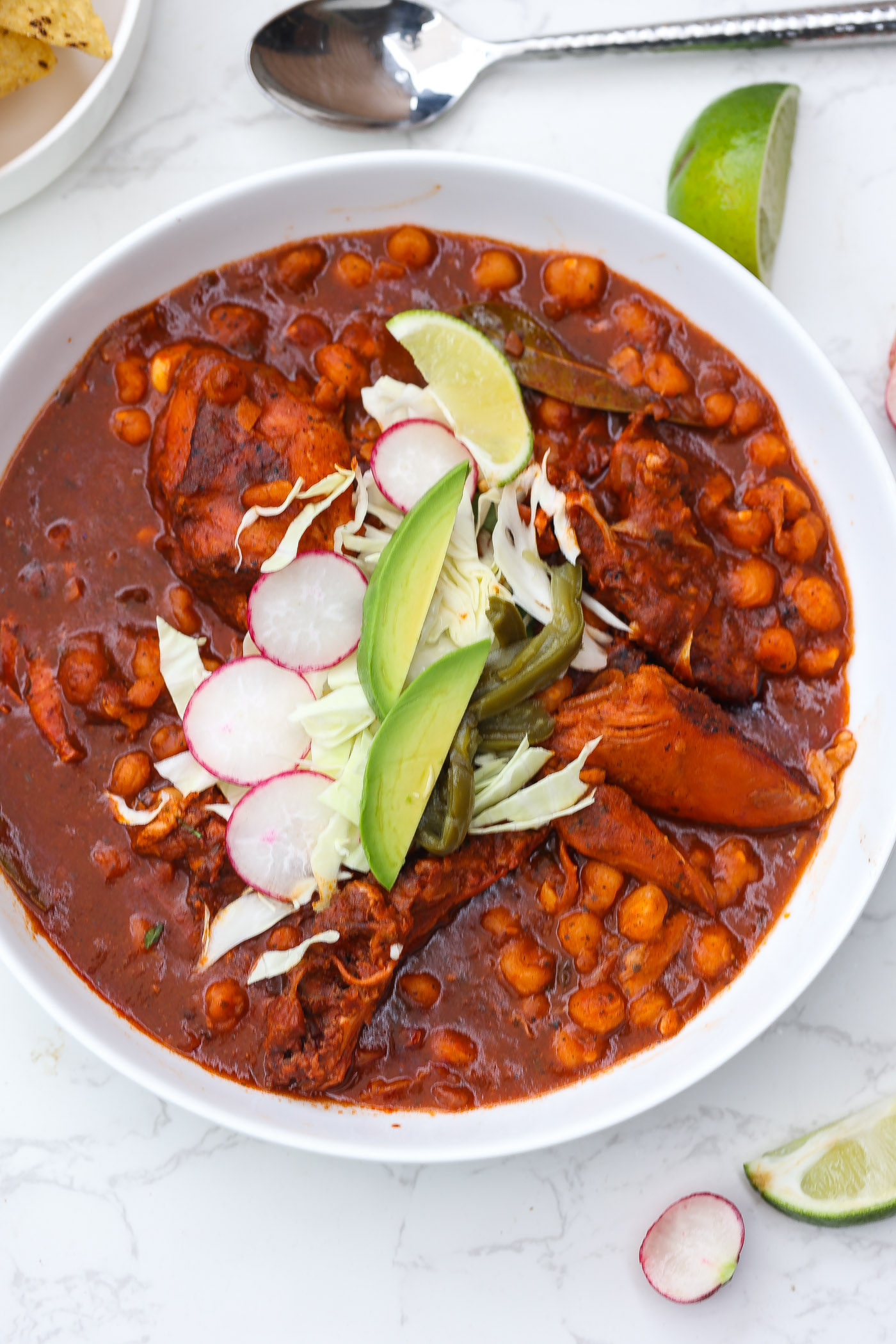 pozole rojo in a white bowl topped with avocado and pickled red onions.