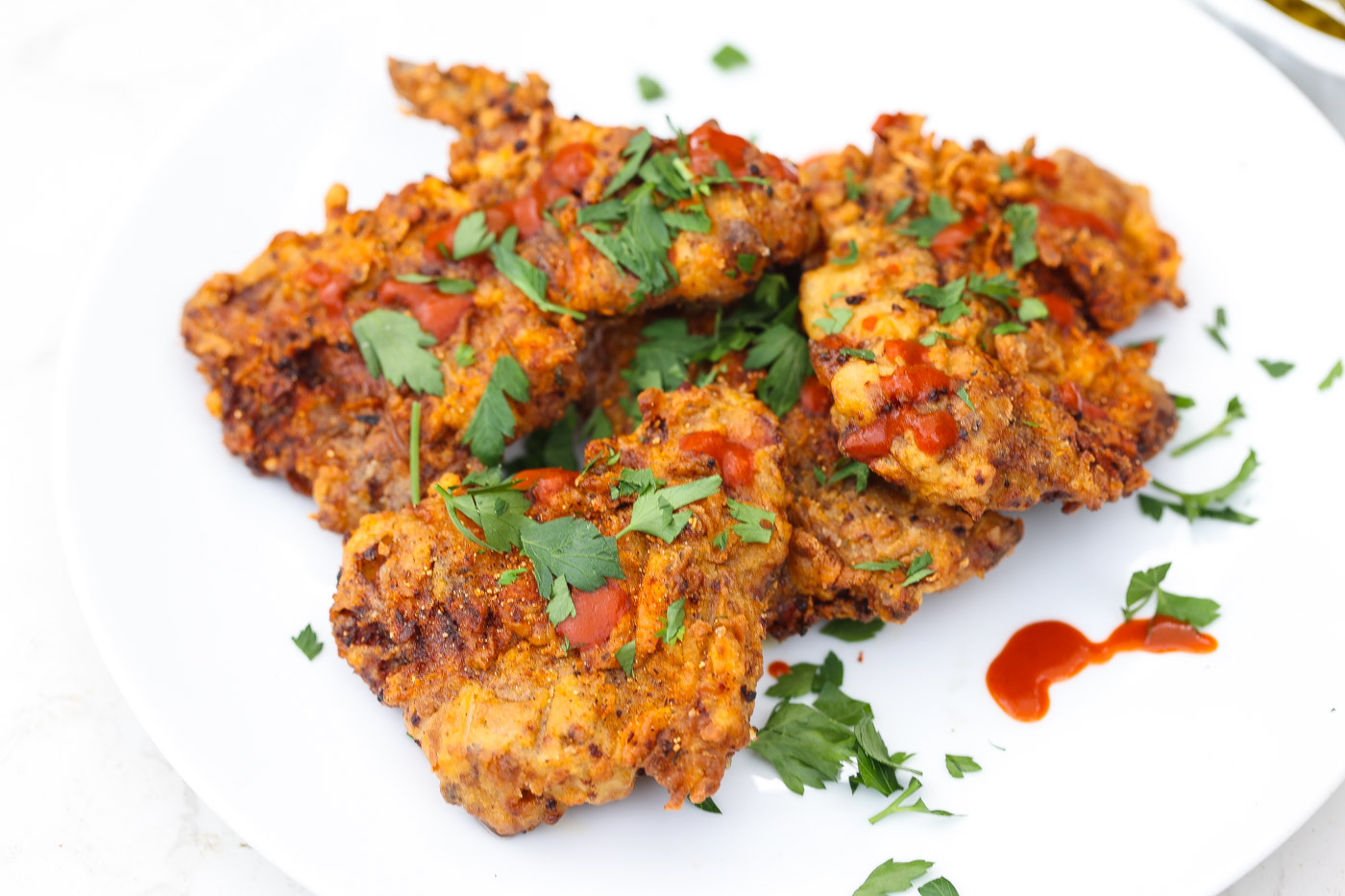 smoked fried chicken on white plate topped with hot sauce and fresh cilantro
