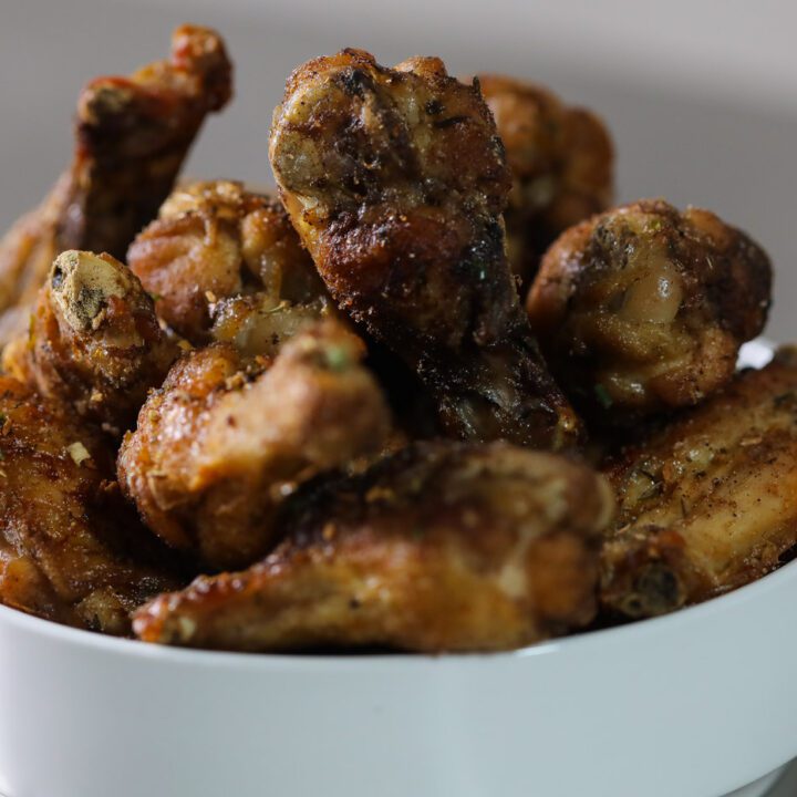 baked jerk wings in a bowl with sliced limes