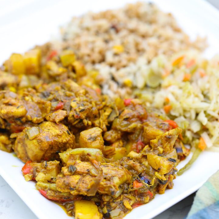 jamaican curry chicken on plate with cabbage and rice.