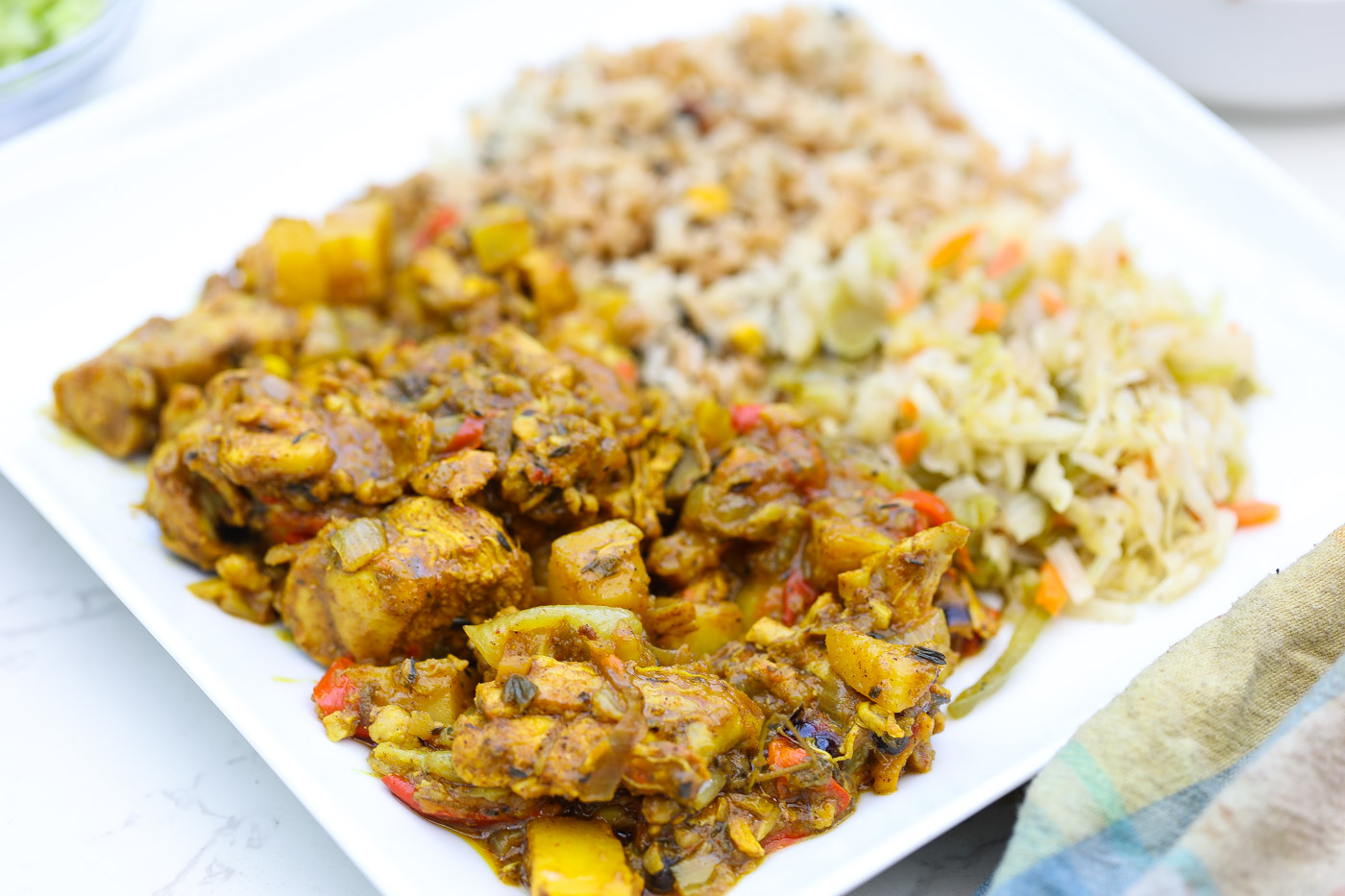 jamaican curry chicken on plate with cabbage and rice.