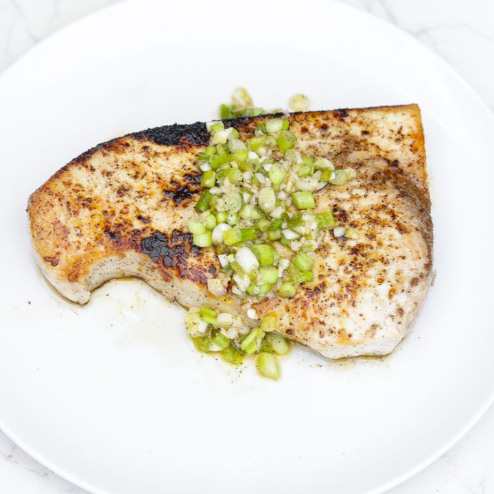 baked swordfish steak on white plate topped with green vinaigrette