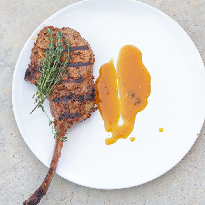 grilled tomahawk pork chop on white plate with yellow sauce.
