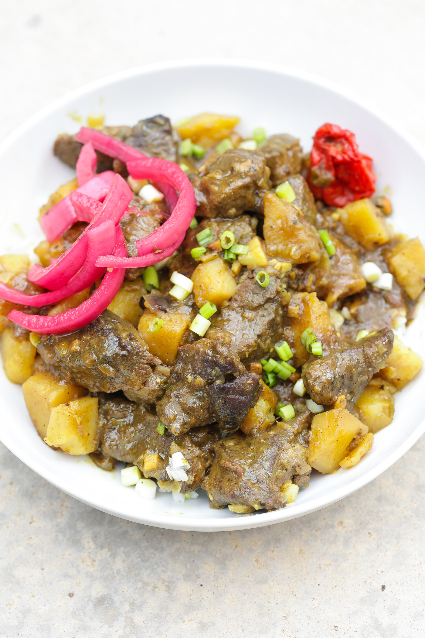 coconut beef curry with potatoes on white plate with pickled red onions