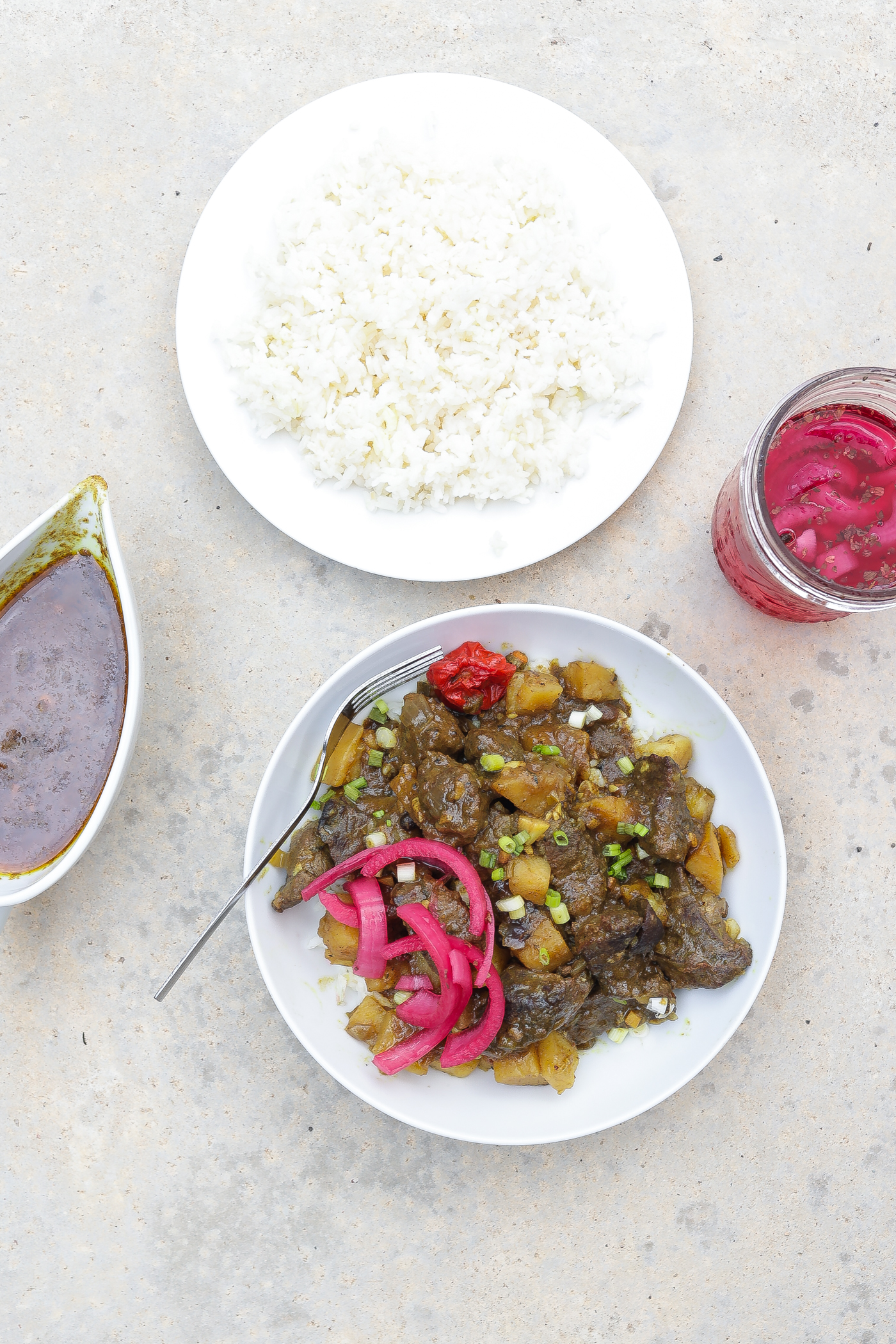 coconut beef curry with potatoes on white plate with pickled red onions