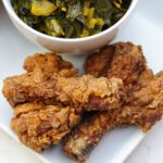 butterflied fried chicken legs on white plate with greens