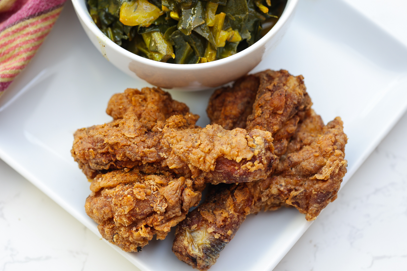 butterflied fried chicken legs on white plate with greens