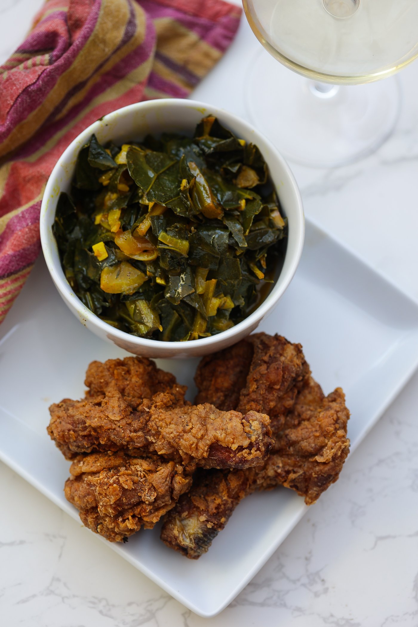 butterflied fried chicken legs on white plate with greens