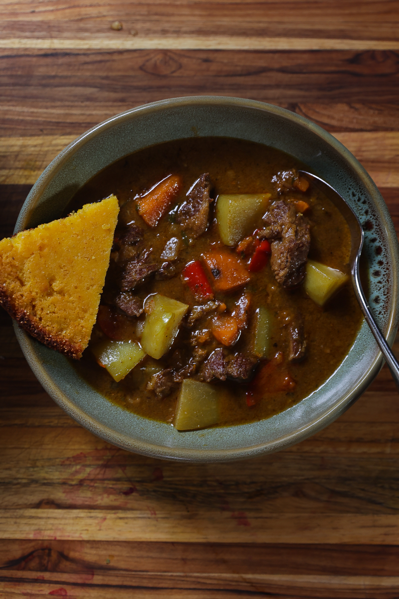 Hungarian goulash (beef stew) in a blue-green bowl with slice of cornbread
