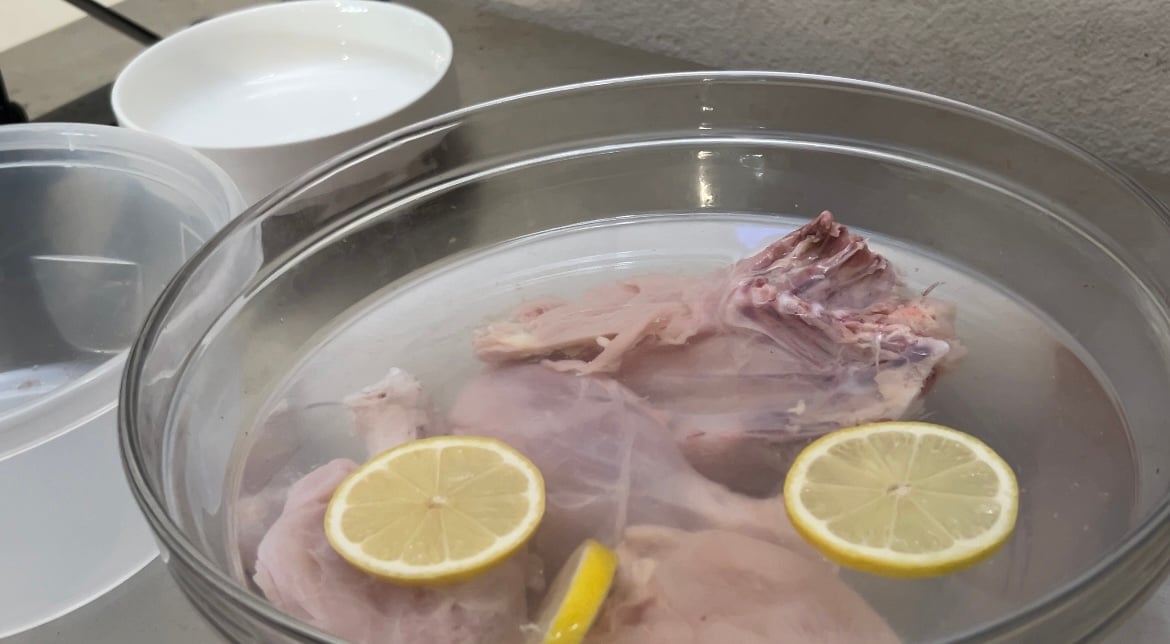 raw chicken in bowl of water with lemons