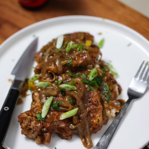 2 smothered chicken thighs sitting on a white plate