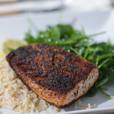 blackened salmon on white plate with rice and greens