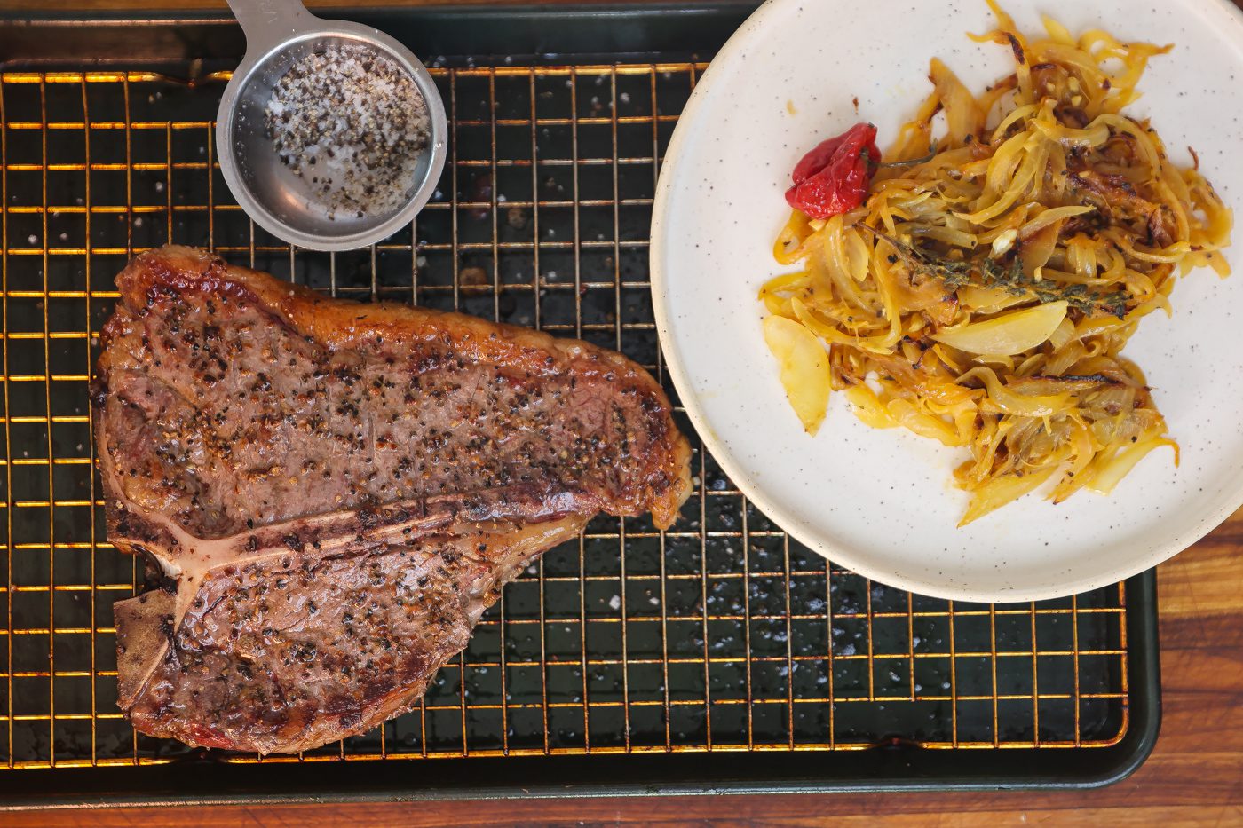 cooked porterhouse steak on tray with yassa onions