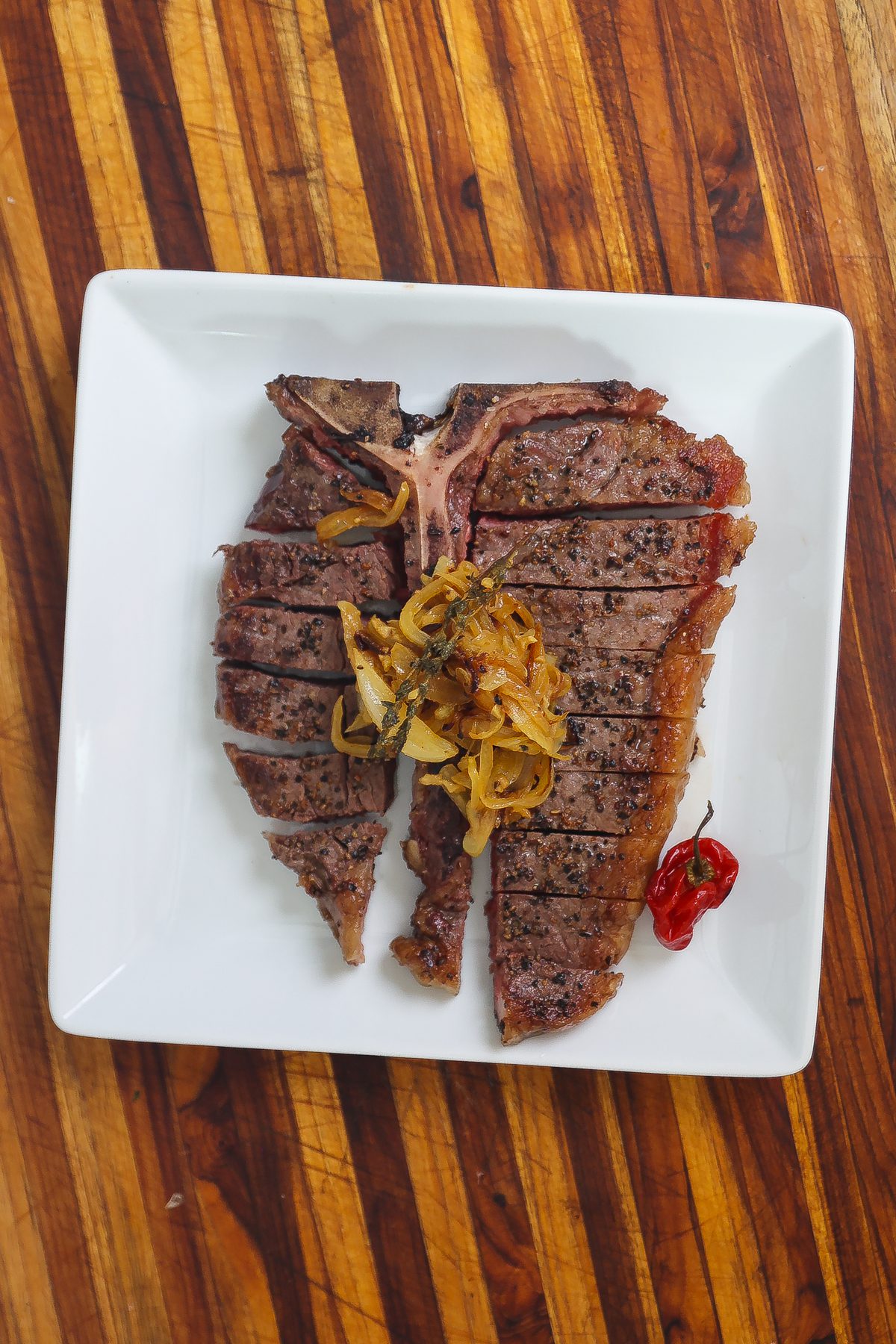porterhouse steak topped with caramelized onions on white plate