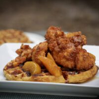 chicken tenders stacked on top of sweet potato waffle and topped with peaches and syrup