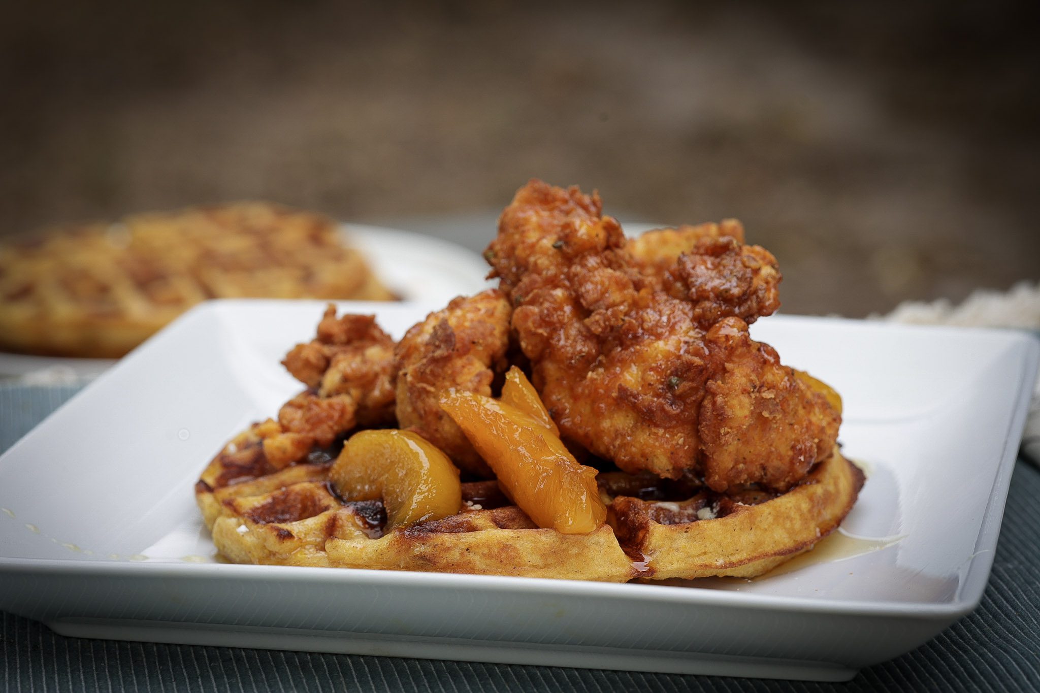 chicken tenders stacked on top of sweet potato waffle and topped with peaches and syrup