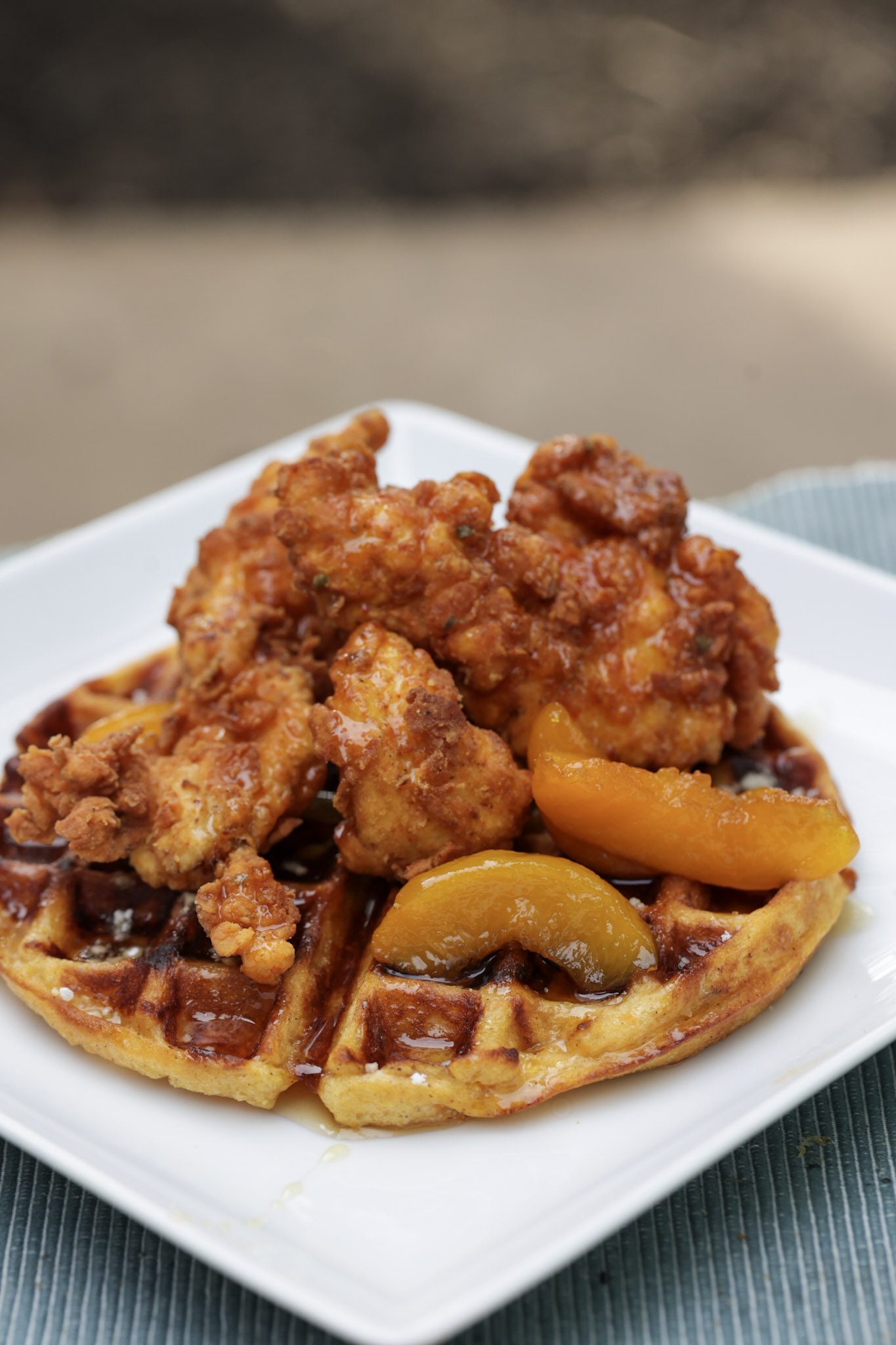 chicken tenders stacked on top of sweet potato waffle and topped with peaches and syrup