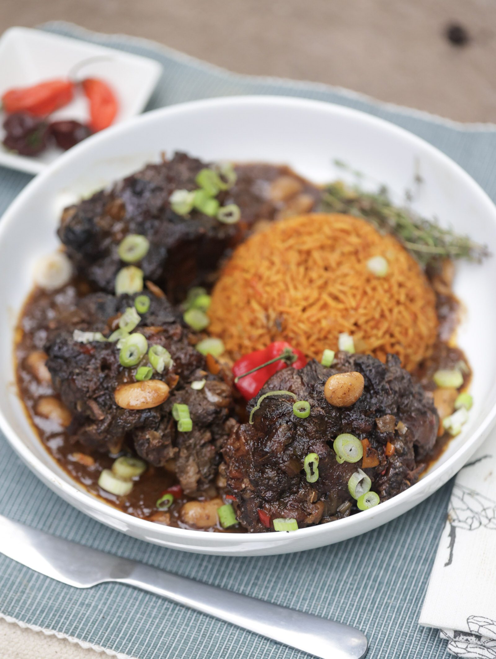 jamaican oxtail with butter beans and jollof rice in white bowl