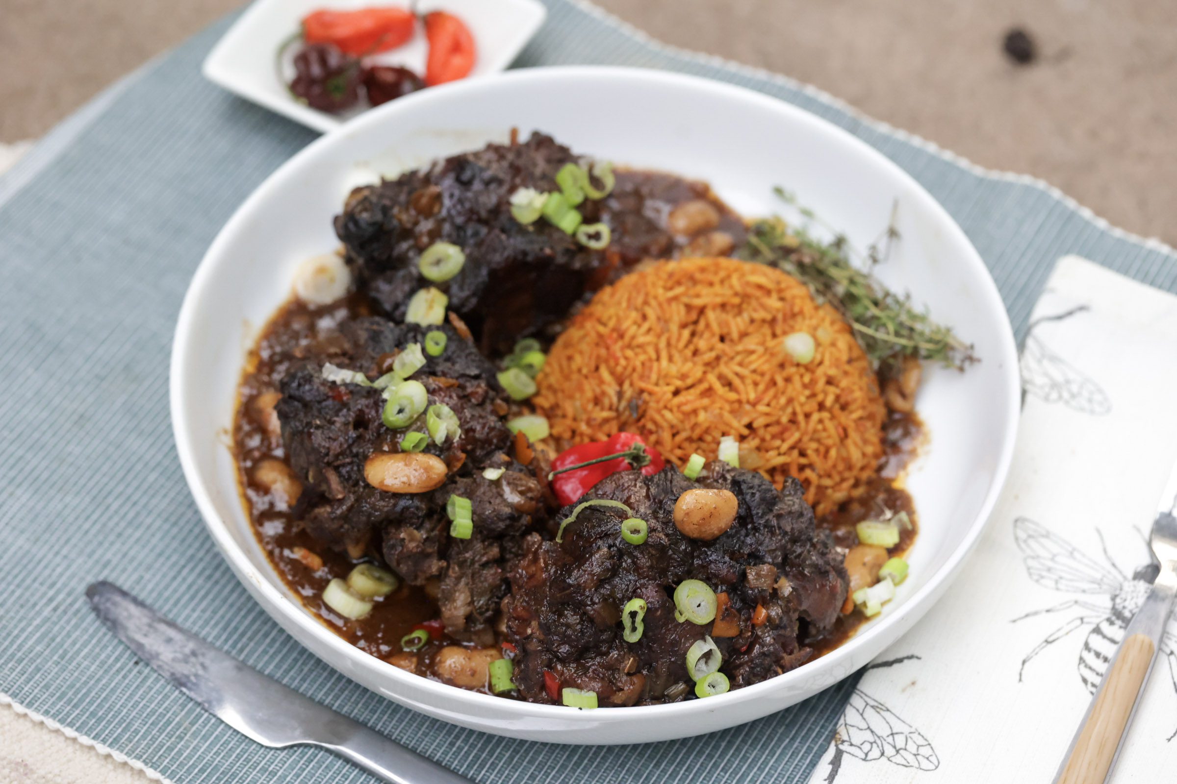 jamaican oxtail with butter beans and jollof rice in white bowl