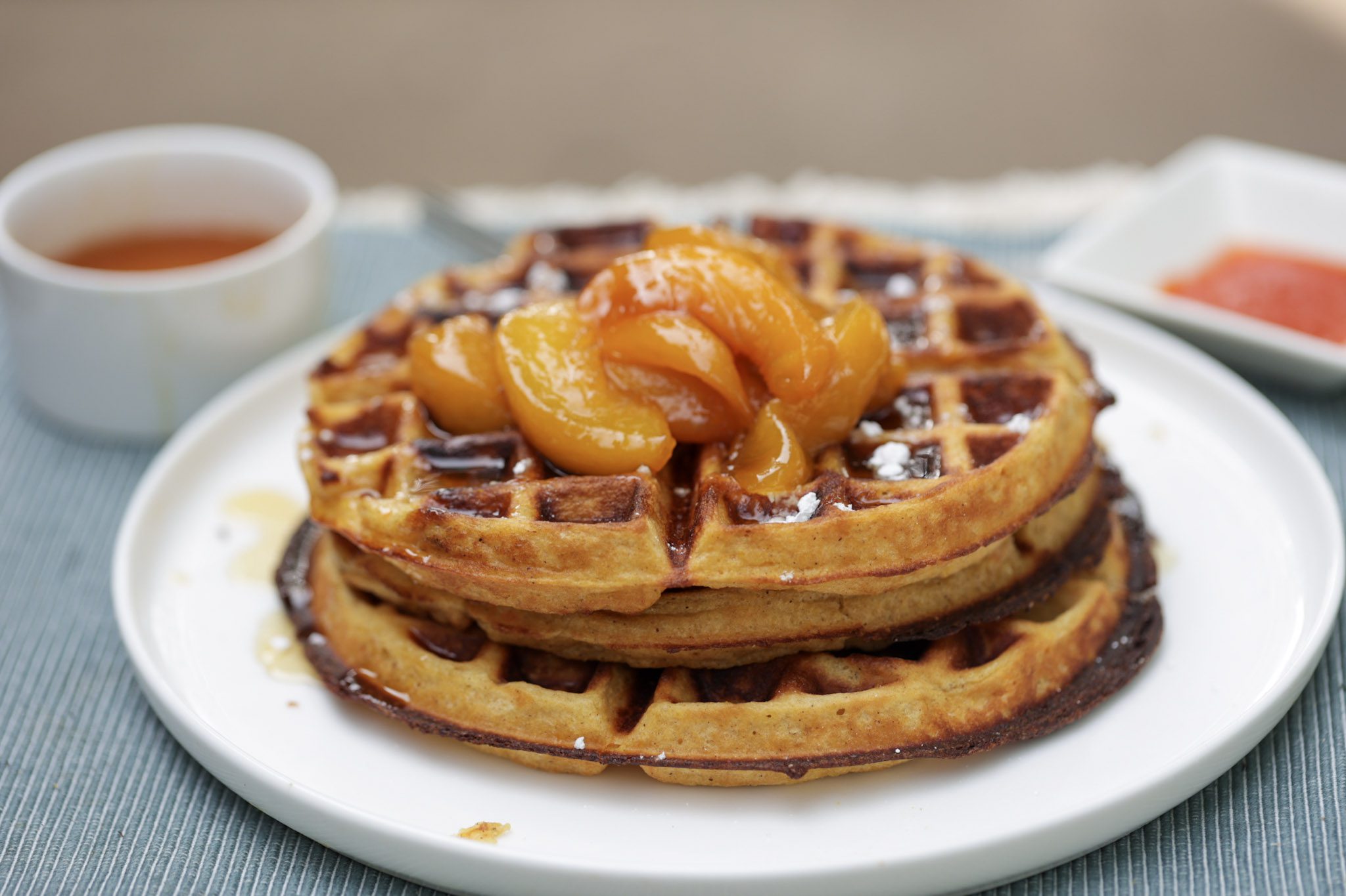 sweet potato waffles stacked on a white plate and topped with maple syrup