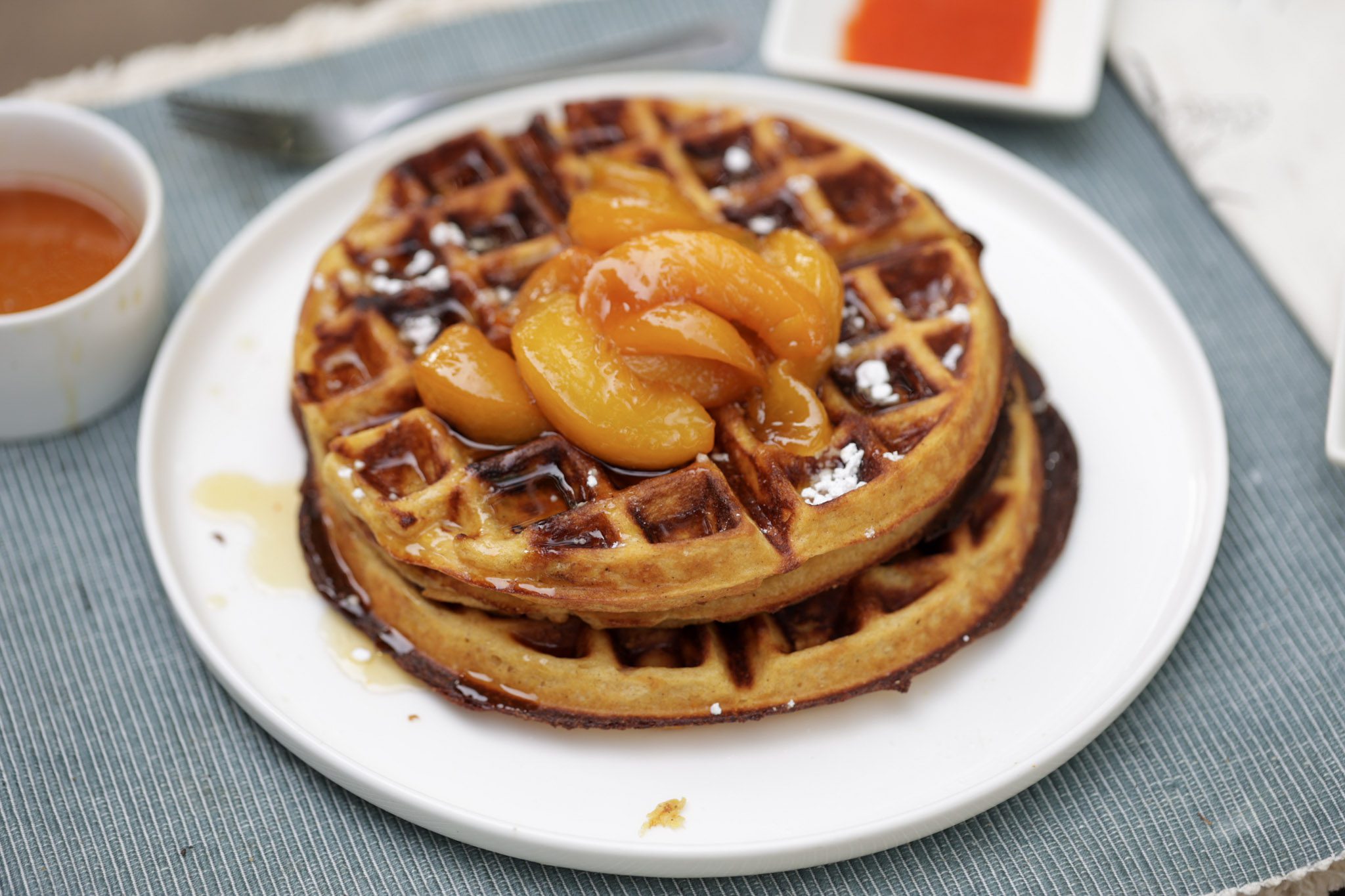 sweet potato waffles stacked on a white plate and topped with maple syrup