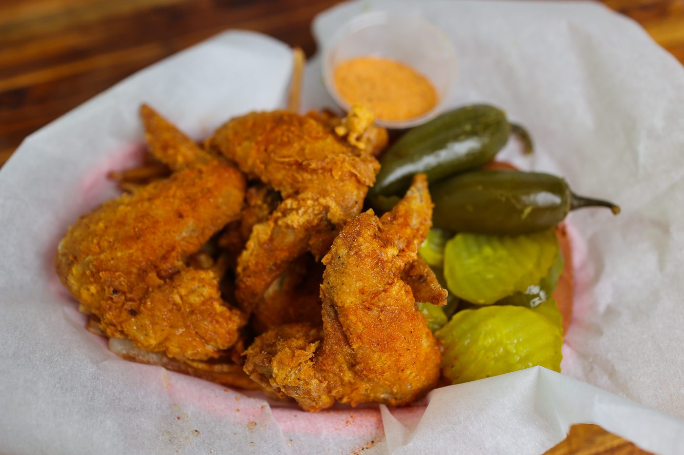 fried chicken wings in a basket with peppers and pickles
