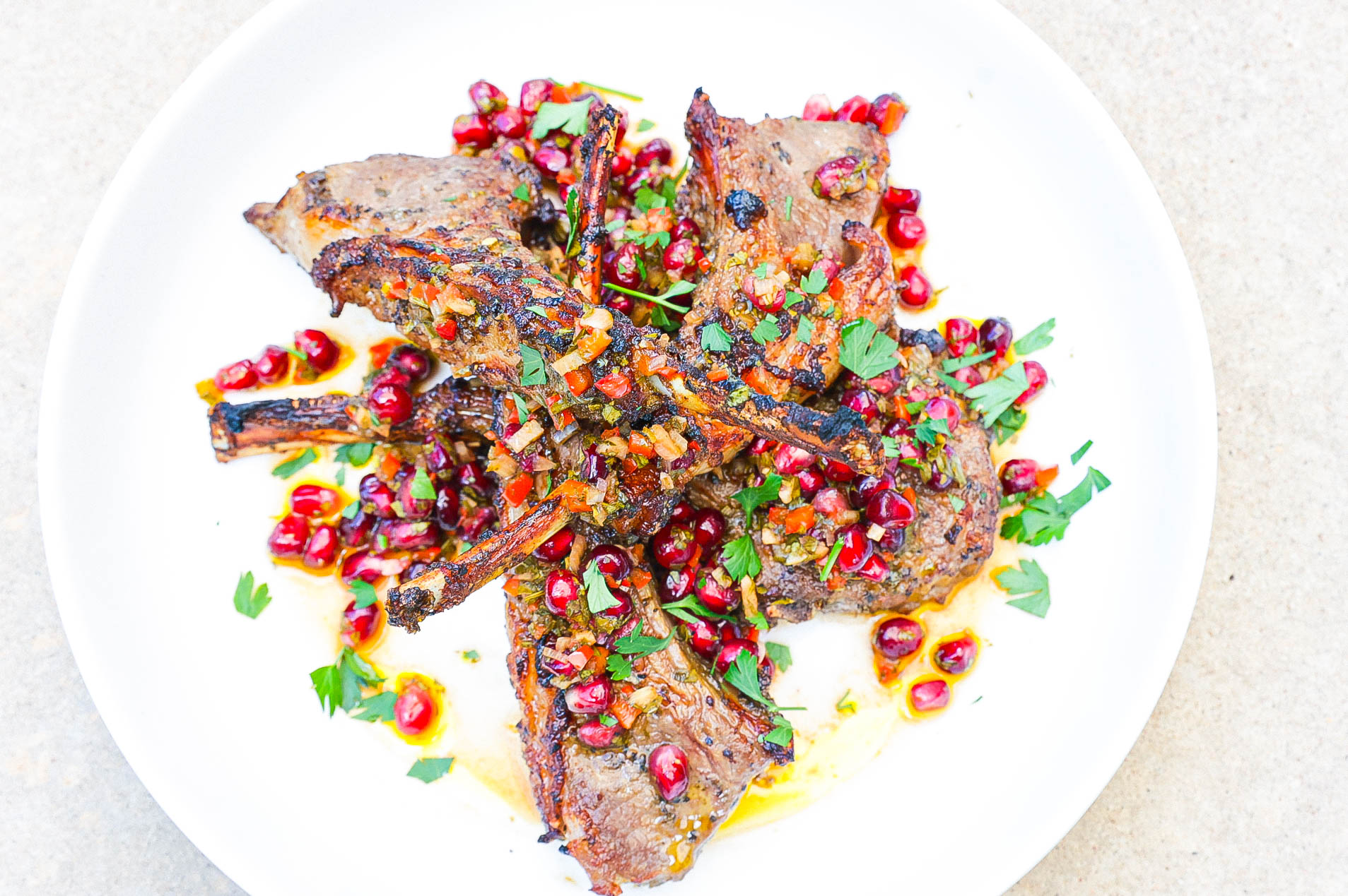 air fryer cooked lamb chops topped with pomegranate chimichurri on white plate
