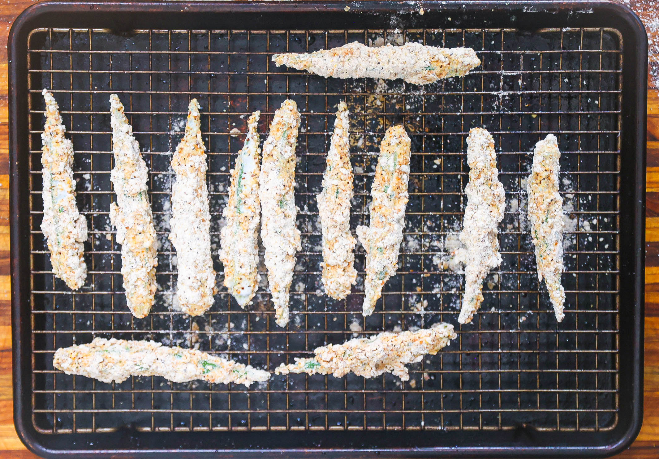 whole okra breaded and resting on wire rack lined baking sheet